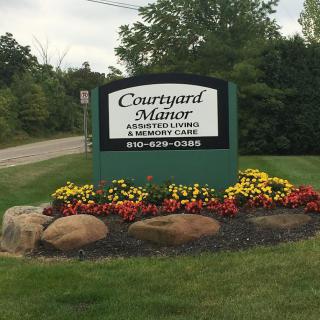 An outdoor sign for Courtyard Manor surrounded by flowers and rocks.