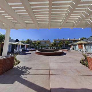 A sunny courtyard featuring a central fountain, surrounded by a pergola and outdoor seating areas.