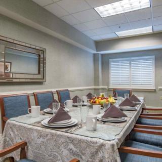 A formal dining room setup with a table elegantly arranged with plates, napkins, and glasses, surrounded by upholstered chairs.