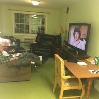 A cozy living room scene with an adult male relaxing on a sofa while watching television.