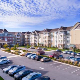 A suburban apartment complex with a spacious parking lot under a clear blue sky.