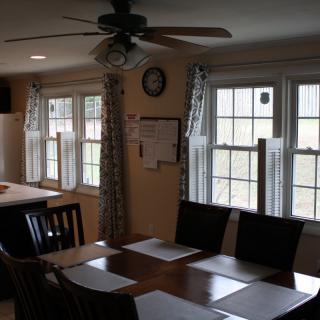 A cozy dining room with a wooden table, surrounded by chairs, and illuminated by natural light from multiple windows.