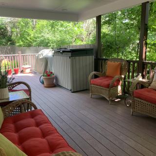 A cozy outdoor patio with wicker furniture and vibrant cushions, surrounded by lush greenery.