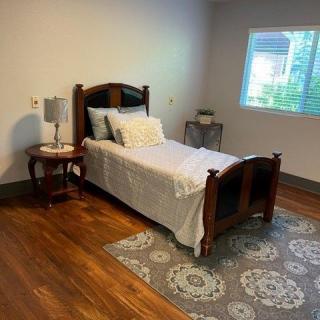 A neatly arranged bedroom with a single bed, nightstand, and a lamp on a wooden floor.