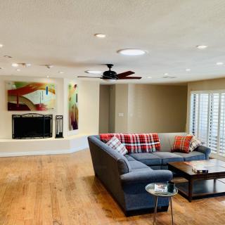 A cozy living room with a sectional sofa, coffee table, and fireplace, featuring wood flooring and modern artwork.