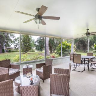 A cozy patio with comfortable seating and ceiling fans, overlooking a lush garden.