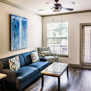 A modern living room featuring a blue sofa, patterned armchair, and a coffee table under a ceiling fan.