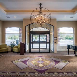 A spacious and elegantly designed lobby featuring a chandelier, comfortable seating, and a piano.