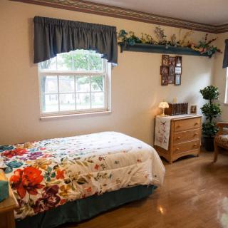 A cozy bedroom with a single bed featuring a floral bedspread, complemented by a dresser and a plant.