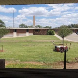 A school yard with a grassy area and trees, framed by cloudy skies.