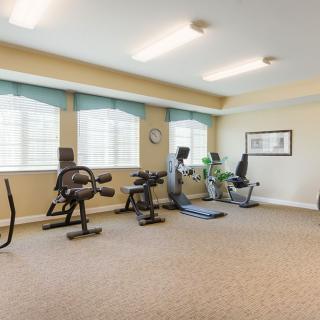A well-lit gym interior with various fitness equipment and large windows.