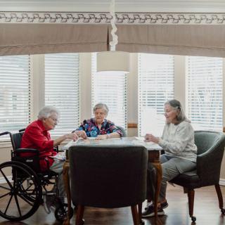 A group of elderly individuals engaging in a social activity around a table in a well-lit room.