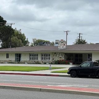 A modern building set against a cloudy sky, featuring well-maintained grass and a nearby sidewalk.