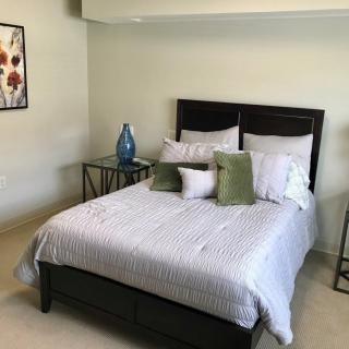 A neatly arranged bedroom with a comfortable bed, decorative pillows, nightstands, and a piece of wall art.