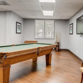 A well-lit game room with a pool table and hardwood flooring.