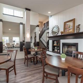 A modern living and dining area featuring a fireplace, wood flooring, and an elegant staircase.