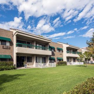 A residential apartment building with balconies and a well-maintained lawn under a partly cloudy sky.