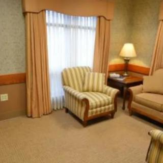 A cozy living room setup with a striped armchair, sofa, lamp on a side table, and draped curtains over a window.