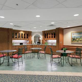 A cozy cafeteria setting featuring round tables and chairs, with wooden cabinetry and soft lighting.