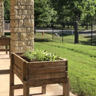 A beautifully crafted wooden planter filled with herbs, situated on a sunny patio.