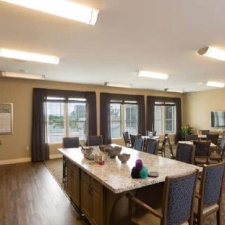 A spacious dining room with large tables and chairs, illuminated by overhead lights and natural light from expansive windows.