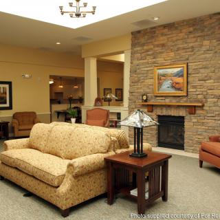 A cozy living room featuring a sofa, armchairs, a fireplace with artwork above it, and a decorative lamp on a side table.