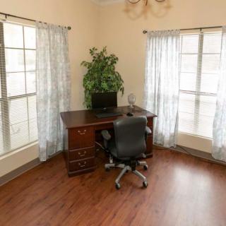 A home office setup with a desk, chair, computer, and a potted plant by the windows with curtains.