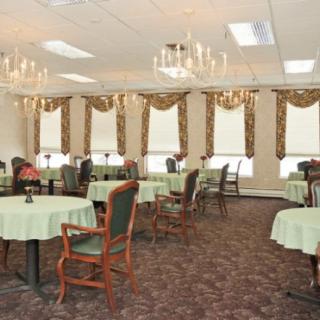 An elegant dining room featuring chandeliers, round tables with green tablecloths, and upholstered chairs.