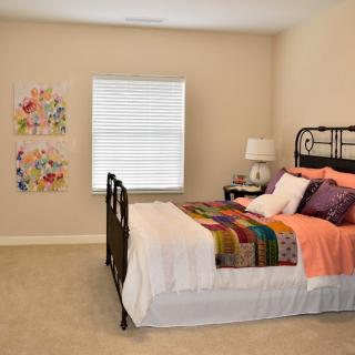 A cozy bedroom with colorful bedding and wall art, featuring a window and bedside lamp.