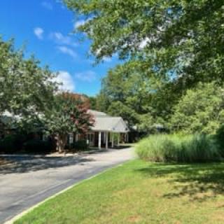 A scenic view of a house surrounded by trees with a driveway leading up, under a clear blue sky.