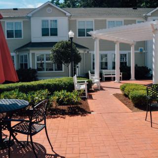 A sunny courtyard features outdoor seating and a pergola, surrounded by a well-maintained garden.