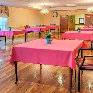 A spacious dining area set up with pink tablecloths and potted plants, featuring wooden floors and warm lighting.