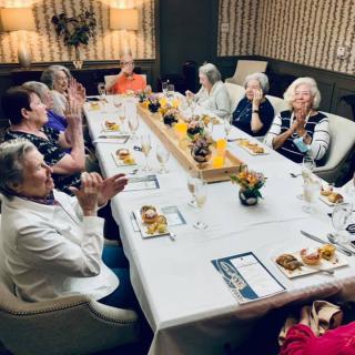 Elderly group enjoying a celebration at a dining table, clapping and sharing a meal.