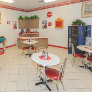 A retro-themed cafe with red and white decor, featuring small round tables and chairs, and vending machines in the corner.