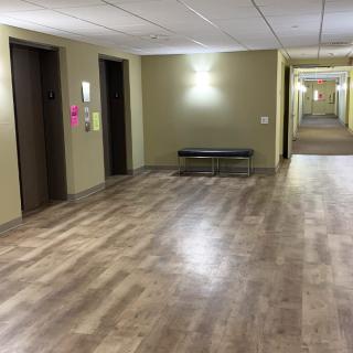 A hotel hallway with elevators and a bench on a wooden floor.