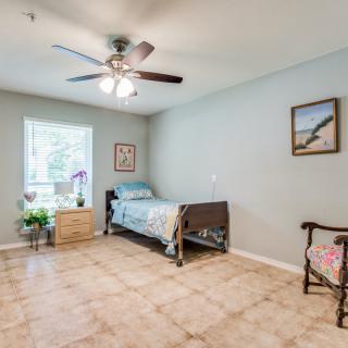 A simple bedroom with a single bed, ceiling fan, and tiled floor.