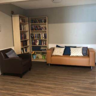 A cozy living room with a sofa, bookshelf, and armchair on a hardwood floor.