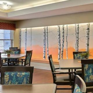 A modern dining area with tables and chairs, featuring an artistic wall mural of birch trees.
