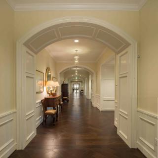 A long hallway with wooden floors and classic arch design, featuring elegant furniture and soft lighting.