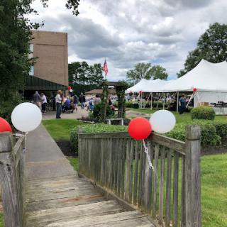 A festive outdoor event featuring tents and colorful balloons along a wooden pathway.