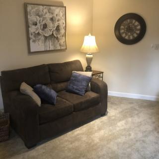 A cozy living room with a sofa, lamp, wall art, and a clock.