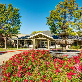 A beautifully landscaped entrance with a blooming garden and a fountain in front of a building.