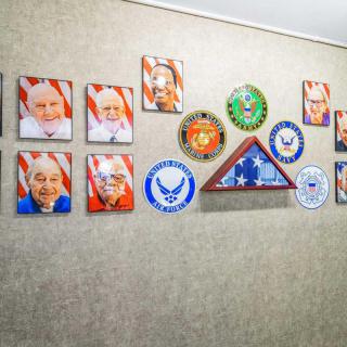 A wall display featuring portraits of veterans, military insignia, and a folded American flag.