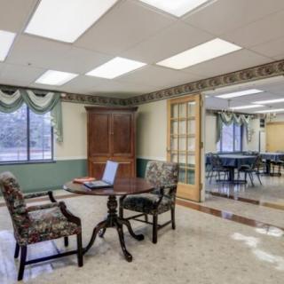 A well-lit office meeting room with a small table and chairs, decorated with curtains and large windows.