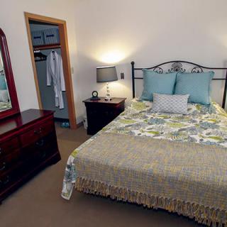 A cozy bedroom with a neatly made bed, bedside lamp, wardrobe, and mirror.
