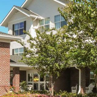 A residential building surrounded by trees, featuring large windows and a mix of brick and siding exterior.