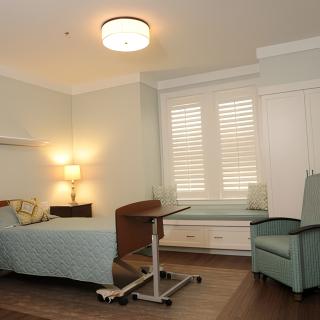 A well-lit medical room with a hospital bed, chair, and side table.