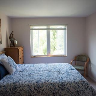 A cozy bedroom with a bed, dresser, and chair, illuminated by natural light from the window.