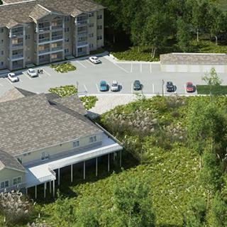 Aerial view of a building complex surrounded by trees, with a parking lot and several cars visible.