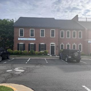 A brick commercial building with parked vehicles in the foreground on a sunny day.